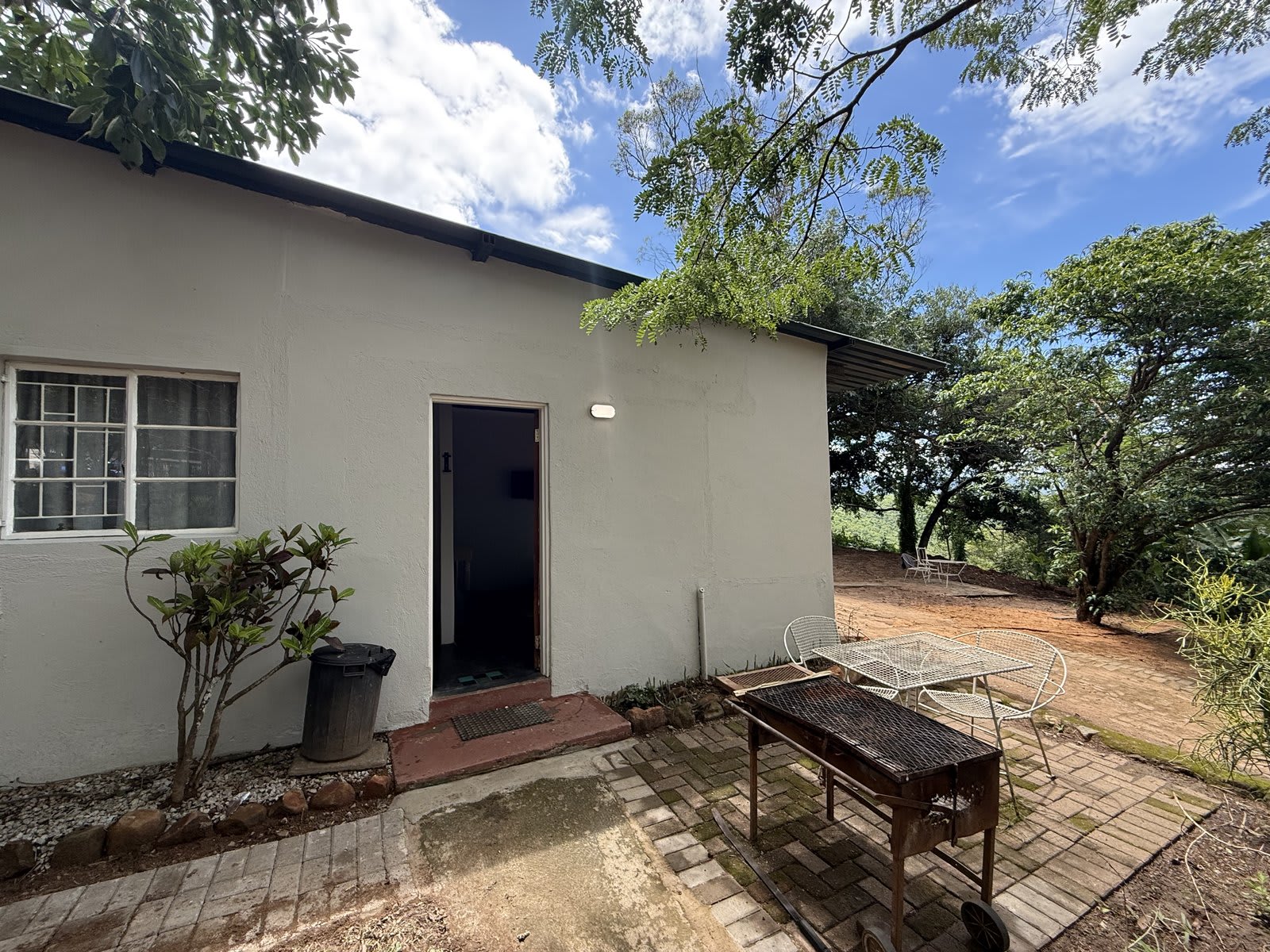 The front of a lodge unit at Kanaan — a brick-paved patio, a built-in braai under shade, and the bushveld just beyond.